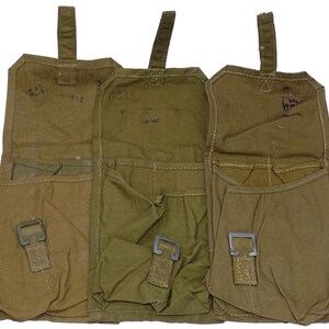May include: Three olive green canvas pouches with metal buckles and top flaps. Each pouch has a rectangular shape with multiple pockets. The pouches are open, revealing the interior. The background is white.