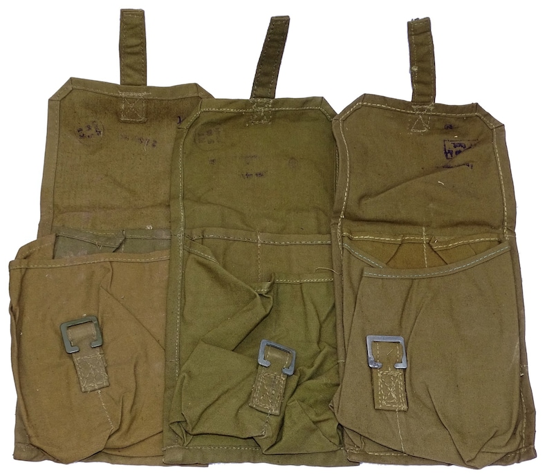 May include: Three olive green canvas pouches with metal buckles and top flaps. Each pouch has a rectangular shape with multiple pockets. The pouches are open, revealing the interior. The background is white.