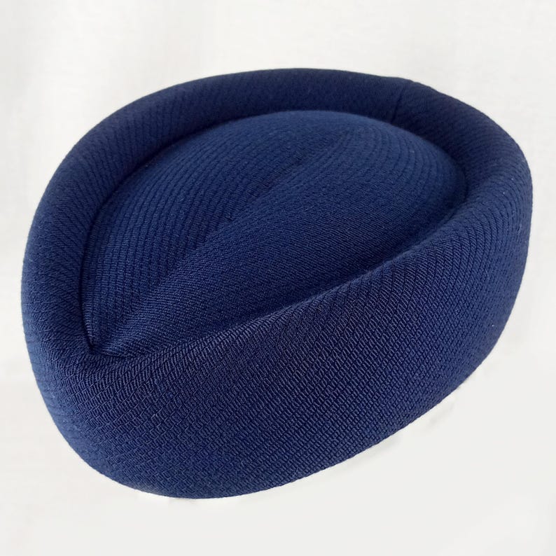 Pu&ograve; includere: Un cappello a scatola blu navy con una corona arrotondata e un tessuto strutturato e a coste. Il cappello ha una forma circolare e un centro leggermente rialzato. Il cappello &egrave; realizzato in un materiale morbido e flessibile.