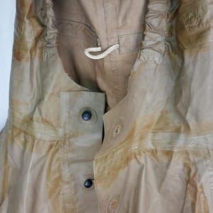 May include: A tan-colored waterproof jacket with a drawstring hood and a button closure. The jacket has a worn and faded appearance, with visible stains and discoloration.
