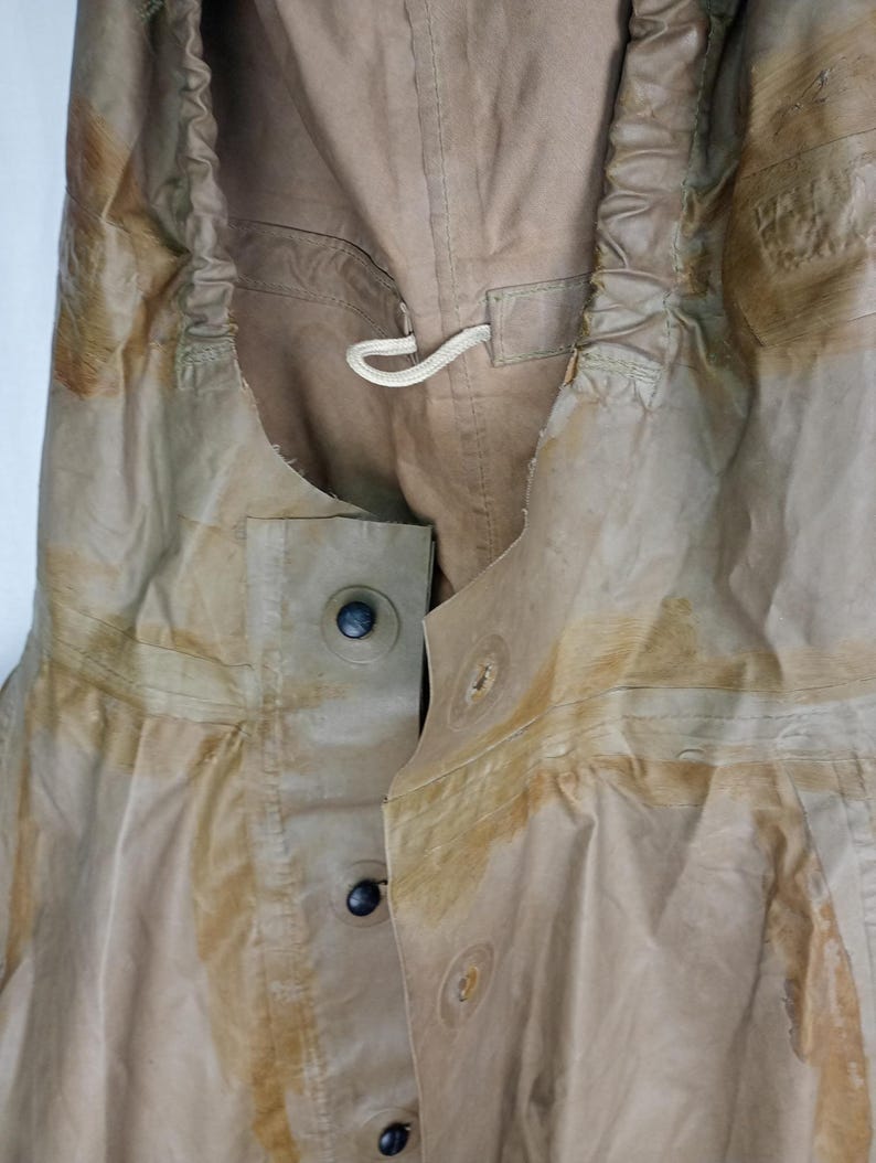 May include: A tan-colored waterproof jacket with a drawstring hood and a button closure. The jacket has a worn and faded appearance, with visible stains and discoloration.