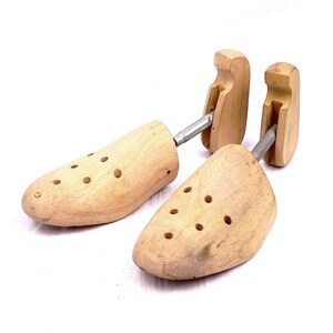 May include: A pair of wooden shoe trees with metal rods connecting the two pieces. The shoe trees have holes for ventilation and are made of light brown wood.