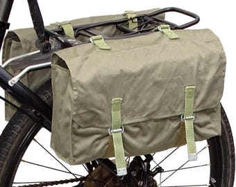 May include: A pair of olive green canvas bike panniers with adjustable straps attached to a black bike rack.