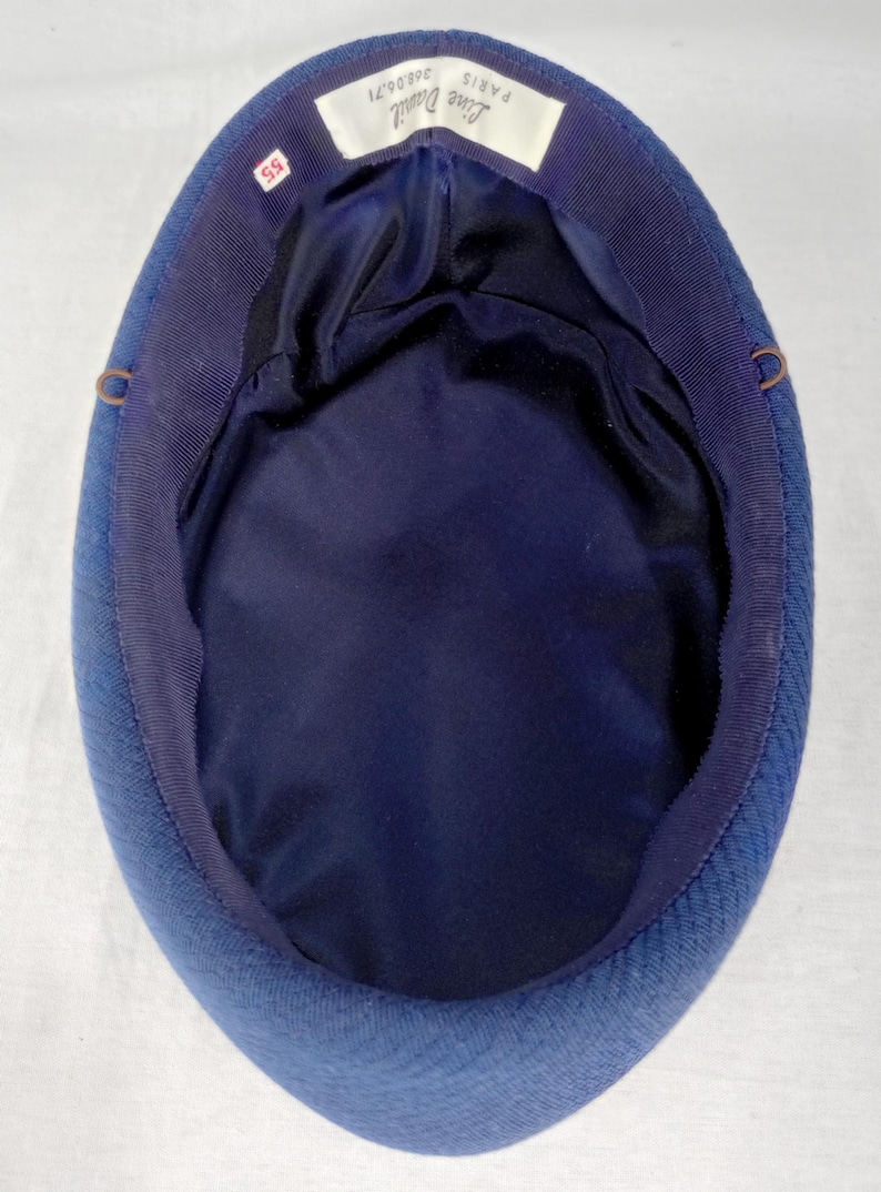 Pu&ograve; includere: Un cappello blu navy con una corona arrotondata e una fodera in raso blu scuro. Il cappello ha un esterno strutturato e un bordo in gros-grain. L'etichetta all'interno recita "Lise Davril Paris" e include la taglia "55".