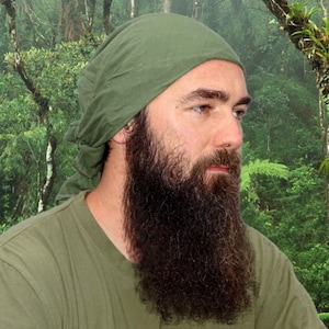 Könnte beinhalten: Ein Mann mit langem Bart trägt ein grünes Bandana und ein grünes Hemd. Er steht vor einem üppigen grünen Wald.