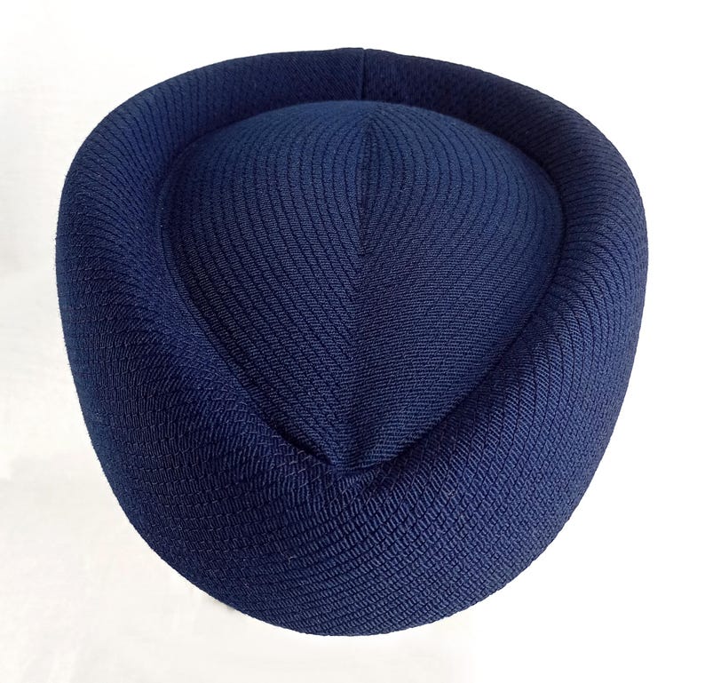 Pu&ograve; includere: Un cappello blu navy con una corona arrotondata e un tessuto strutturato. Il cappello ha un bordo circolare e una parte superiore leggermente rialzata. Il cappello &egrave; realizzato in un materiale tessuto ed &egrave; di colore uniforme.