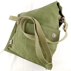 May include: A green canvas bag with a long strap and a flap closure. The bag has a small pocket on the front and a metal buckle on the side.
