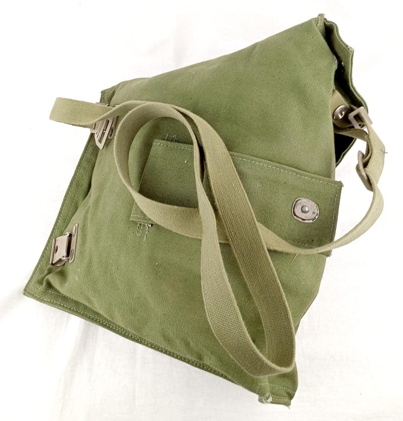 May include: A green canvas bag with a long strap and a flap closure. The bag has a small pocket on the front and a metal buckle on the side.