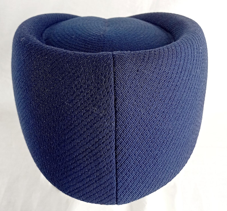 Pu&ograve; includere: Un cappello blu navy con una corona arrotondata e una base cilindrica. Il cappello ha un aspetto in tessuto strutturato e tessuto. Il cappello &egrave; di colore pieno e sembra essere fatto di un materiale robusto.