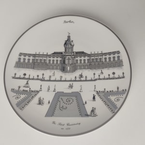 Könnte beinhalten: Ein weißer Keramikteller mit einer Schwarzweißillustration eines Schlosses mit Garten. Der Text "Berlin" und "The Schloss Charlottenburg - 1770" ist auf dem Teller gedruckt.