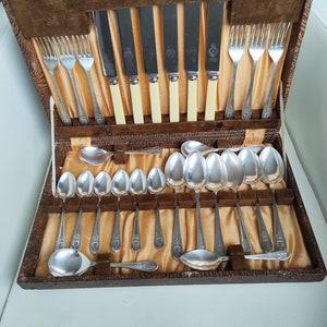 Può includere: Una scatola di legno con un rivestimento in velluto marrone contiene un set di posate d'argento. Le posate includono coltelli, forchette e cucchiai. I coltelli hanno manici in avorio.