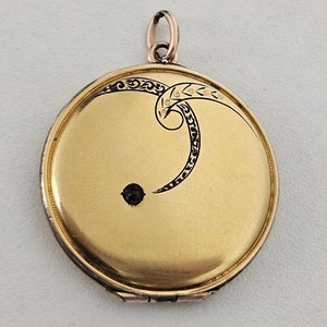 Può includere: Un medaglione d'oro con un design a spirale nero e oro e una piccola pietra di rubino.