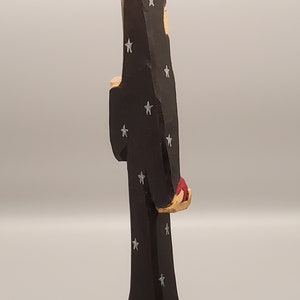 Puede incluir: Una figurita de madera de una persona que lleva una t&uacute;nica negra con estrellas blancas. La figurita sostiene un objeto rojo en su mano derecha.