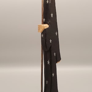 Puede incluir: Una figurita de madera de una persona que lleva una t&uacute;nica negra con estrellas plateadas. La figurita sostiene un bast&oacute;n de madera.