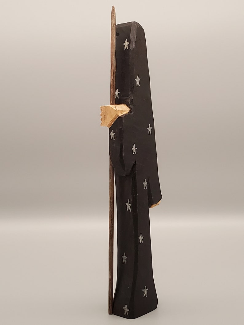 Puede incluir: Una figurita de madera de una persona que lleva una t&uacute;nica negra con estrellas plateadas. La figurita sostiene un bast&oacute;n de madera.