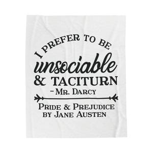 Puede incluir: Manta blanca con texto negro. El texto dice "I PREFER TO BE unsociable & TACITURN - Mr. Darcy" y "PRIDE & PREJUDICE BY JANE AUSTEN". La manta tiene un aspecto suave y texturizado.