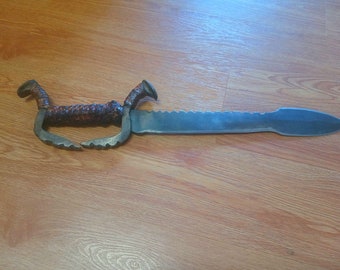 May include: A handmade sword with a brown leather wrapped handle and a serrated blade. The blade is pointed and has a slight curve.