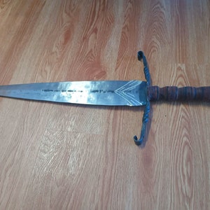 May include: A silver sword with a brown leather wrapped handle and a twisted metal guard. The sword is lying on a wooden surface.