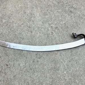 May include: A curved metal sword featuring a long, silver-toned blade that terminates in a split, two-pronged tip. The handle is wrapped in black cord and includes a dark, curved metal hand guard that extends toward the pommel.