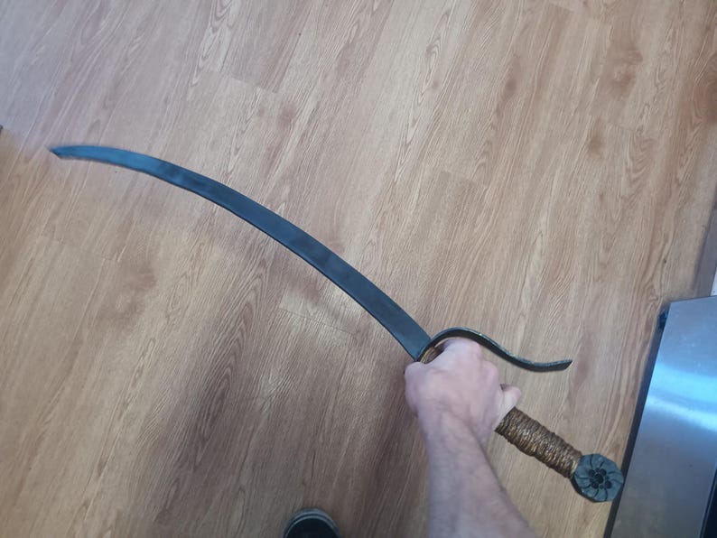 May include: A curved, black metal sword with a textured, wrapped handle. The blade has a slight curve and a pointed tip. The handle is wrapped in a brown material and has a decorative end.