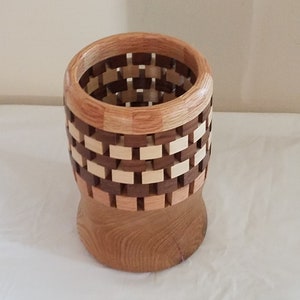 May include: A wooden vase with a checkered pattern, made from different types of wood. The vase is brown, beige, and light brown.