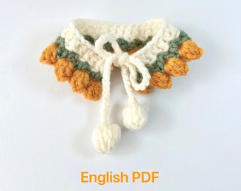 Puede incluir: Un collar de ganchillo con base blanca, detalles verdes y naranjas, y dos pompones blancos. El collar tiene un cierre de lazo. PDF en inglés.