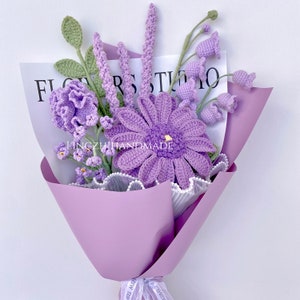 Op de afbeelding: Een boeket van gehaakte bloemen in tinten paars en groen, verpakt in lavendelpapier met een wit lint. De bloemen omvatten een grote madeliefje, kleinere klokvormige bloemen en takjes lavendel. Het boeket is gelabeld met "Flower Studio" en "Lingzhihandmade".