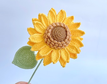 May include: A crocheted sunflower with a green leaf stem. The sunflower is yellow with a brown center.