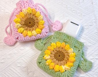 May include: Two crocheted sunflower pouches, one pink and one green, with a white AirPod case inside the green pouch.