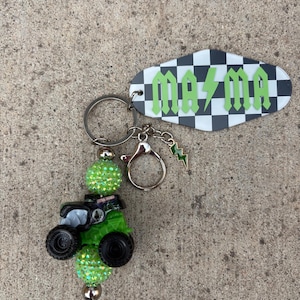 May include: A keychain with a green monster truck charm, sparkling green beads, and a tag with the word "Mama" in green lettering on a black and white checkered background. Includes a small green lightning bolt charm.