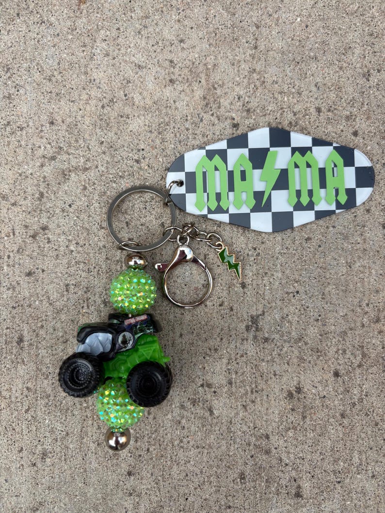 May include: A keychain with a green monster truck charm, sparkling green beads, and a tag with the word "Mama" in green lettering on a black and white checkered background. Includes a small green lightning bolt charm.