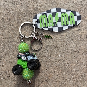 May include: Keychain with a green monster truck charm, green glitter beads, and a tag with the word "MAMA" in green lettering on a black and white chequered background. Includes a silver keyring and a lightning bolt charm.