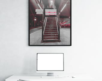 May include: A framed wall art print featuring a black and white photograph of a train station staircase with red accents. The image shows a central set of stairs leading upward, a digital train schedule display, and overhead lighting fixtures.