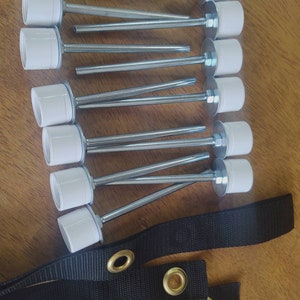 May include: Ten white plastic tent stakes with metal rods and black straps with metal eyelets.