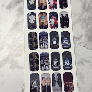 May include: A sheet of nail art stickers featuring various images. Designs include hockey players, couples, and the text "Heated Rivalry." The stickers are in a variety of colors, including black, white, red, and blue.
