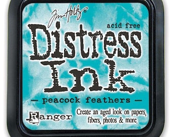 May include: Square ink pad with a black border, featuring the words "Distress Ink" in dark letters over a teal background. The text "peacock feathers" is below the main text, with additional text that reads "Create an aged look on papers, fibers, photos & more."