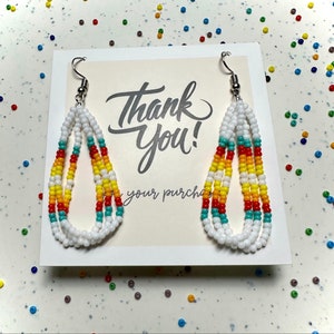 May include: White beaded teardrop earrings with turquoise, yellow, and red accents. The earrings are displayed on a card that says "Thank You!" in script. The earrings have silver-colored hooks.