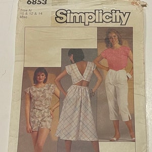 Pode incluir: Padrão de costura Simplicity número 6853 para os tamanhos 10, 12 e 14. O padrão inclui três roupas diferentes: uma blusa branca com um detalhe nas costas em forma de cruz e uma saia xadrez, uma blusa rosa com calças brancas e uma blusa de estampa floral com shorts combinando.
