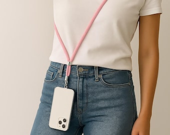 May include: A light pink phone lanyard with a silver-toned clasp holding a white phone case. The lanyard is worn around the neck, and the phone hangs at the waist. The person is wearing a white t-shirt and blue jeans.