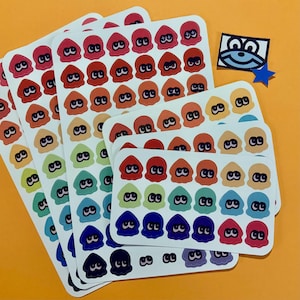 Puede incluir: Hojas de pegatinas coloridas con personajes de calamares de dibujos animados en varios colores, incluyendo rojo, naranja, verde, azul y morado. También hay una pequeña cara de dibujos animados y una estrella azul. Fondo naranja.