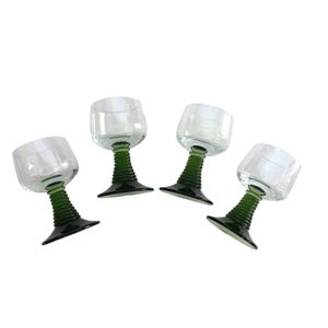 May include: A set of four wine glasses, each featuring a clear, rounded bowl and a distinctive dark green stem with a ribbed, textured design that tapers down to a wide, flat base. The glasses are arranged in a group against a plain white background.