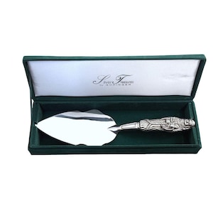 May include: A silver-plated cake server with a decorative handle featuring a sculpted figure, presented in a dark green velvet-lined box. The interior lid displays the text Silver Treasures by GODINGER in elegant black script lettering.