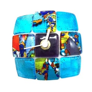 May include: A unique, square-shaped wristwatch with a mosaic design. The watch features a dark purple square center with white hands and a gold-colored bezel. The surrounding squares are a mix of blue, orange, yellow, and green glass.