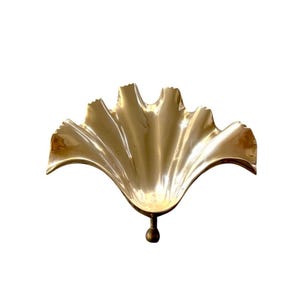 May include: A polished brass bowl shaped like a fan or a ginkgo leaf with a smooth, reflective surface and scalloped edges. The bowl features a single, small, spherical pedestal base at the bottom, providing a stable point of support.