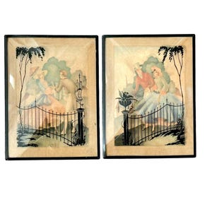 May include: Two framed vintage prints featuring romantic scenes with figures in a garden setting. The artwork includes black silhouette details of trees, fences, and decorative posts. The prints are in black frames.