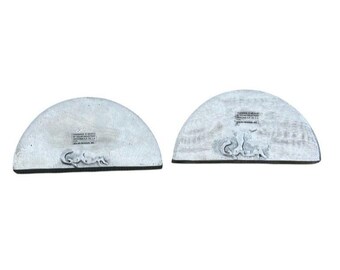 May include: Two half-circle ceramic coasters with a white glaze. The coaster on the left has a small label with text. The coaster on the right has a design of a squirrel.