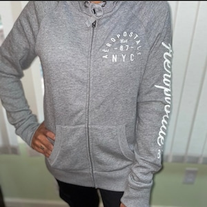 May include: A gray zip-up hoodie with the AeroPostale logo on the chest and sleeve. The logo on the chest is a circular design with the words "AEROPOSTALE Est. - 87 - NYC". The sleeve has the word "AeroPostale" printed vertically.