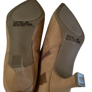 K&ouml;nnte beinhalten: Ein Paar hellbraune Stiefeletten mit spitzer Zehenpartie und kleinem, quadratischem Absatz. Die Sohlen sind dunkler braun. Der Text "NNZ-005 8M FABRIC UPPER/OUTSOLE BAL MAN MADE MATERIAL MADE IN CHINA" ist auf der Sohle zu sehen.