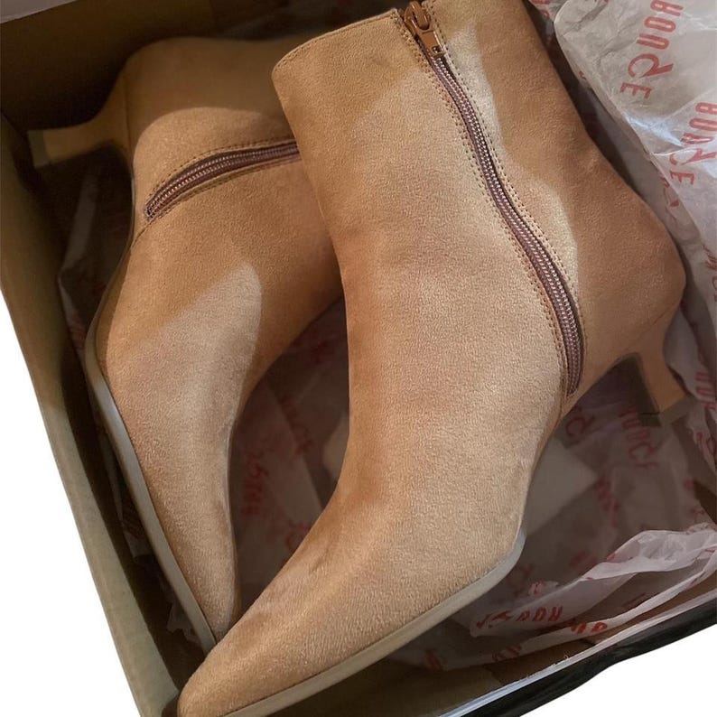 K&ouml;nnte beinhalten: Ein Paar hellbraune Wildleder-Ankle Boots mit spitzer Zehenpartie und kleinem Absatz. Die Stiefel haben einen seitlichen Rei&szlig;verschluss und befinden sich in einer Box.