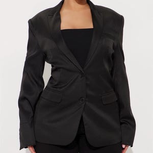 Puede incluir: Un blazer negro con cierre de un solo botón y dos bolsillos delanteros. El blazer tiene un diseño de solapa clásico y mangas largas. La prenda está hecha de un material liso, posiblemente satinado.